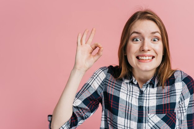 Mujer sonriente haciendo el signo bien con fondo rosa