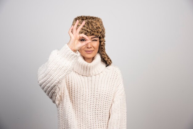 Una mujer sonriente en un hermoso sombrero haciendo bien los ojos gesto mirando a través de los dedos.