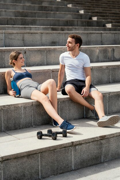 Mujer sonriente y hombre descansando sobre pasos mientras hace ejercicio