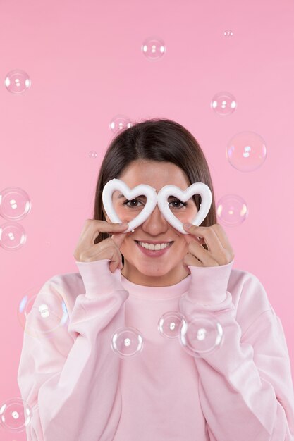 Mujer sonriente joven con los corazones decorativos entre las burbujas de jabón