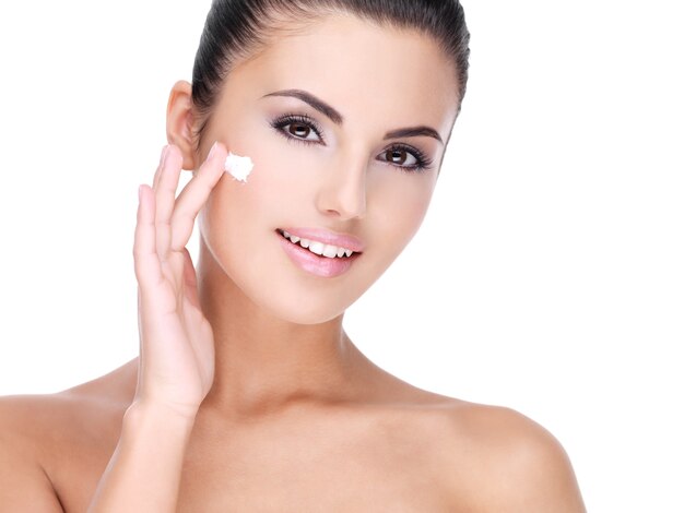 Mujer sonriente joven con crema cosmética en un rostro bastante fresco - aislado en blanco