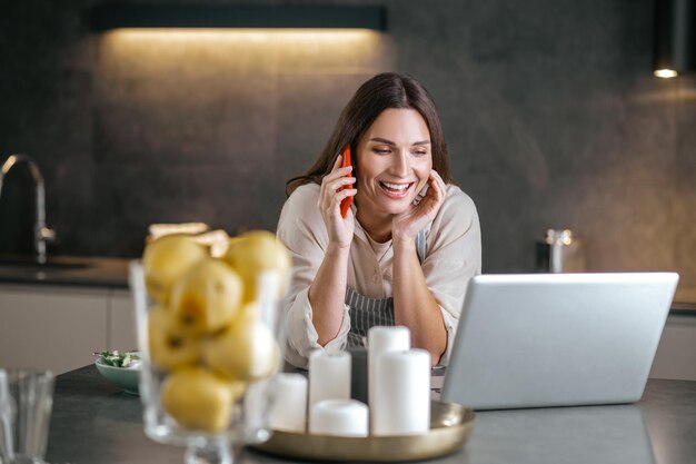 Mujer sonriente joven hablando por teléfono en la cocina