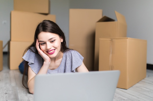 Mujer sonriente joven con laptop en casa nueva buscando maestro de reparación, espacio de copia, concepto de movimiento