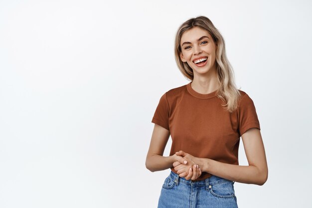 Mujer sonriente joven profesional, tomados de la mano juntos en el pecho, mirando amistoso, de pie en camiseta en blanco