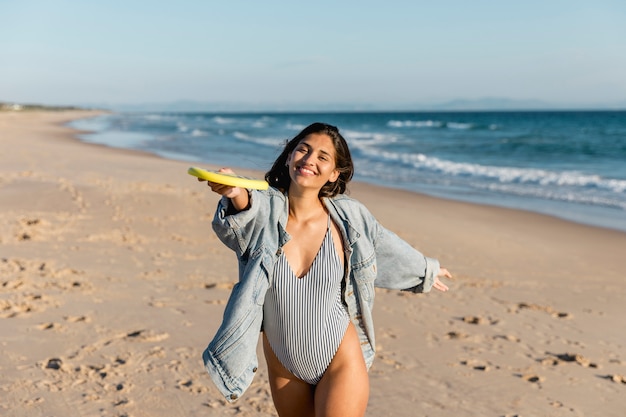 Mujer sonriente joven que juega el disco volador en la costa