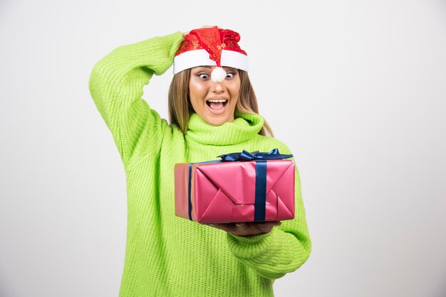 Mujer sonriente joven que sostiene un regalo de Navidad festivo.