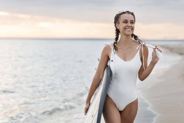 mujer sonriente joven con tabla de surf al aire libre