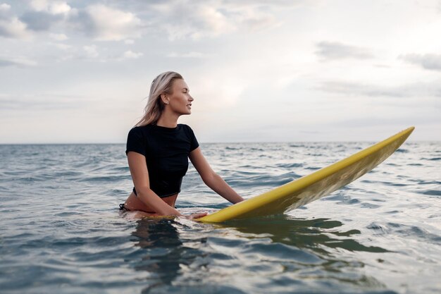 mujer sonriente joven con tabla de surf al aire libre