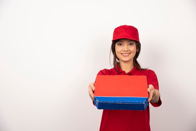 Mujer sonriente joven en uniforme rojo repartiendo pizza en caja.