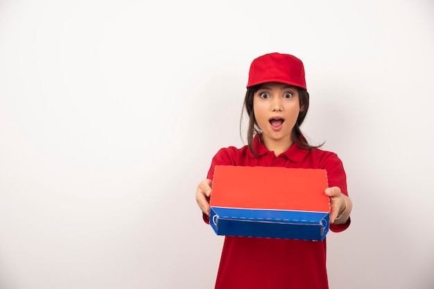 Mujer sonriente joven en uniforme rojo repartiendo pizza en caja.