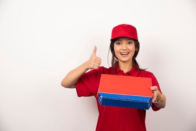 Mujer sonriente joven en uniforme rojo repartiendo pizza en caja.