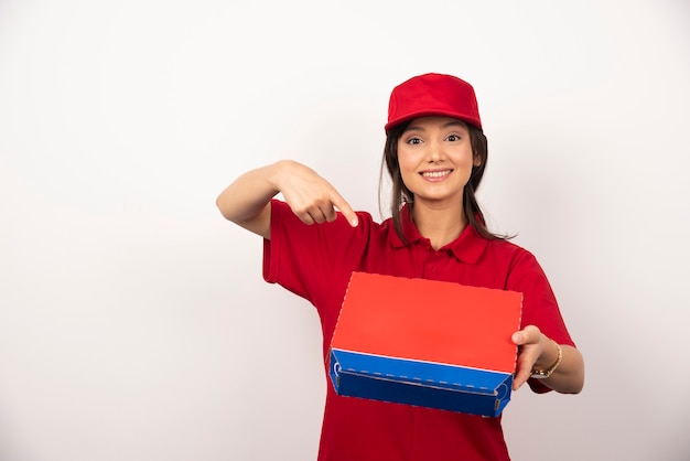 Mujer sonriente joven en uniforme rojo repartiendo pizza en caja.