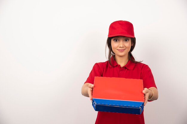 Mujer sonriente joven en uniforme rojo repartiendo pizza en caja.