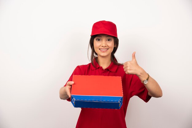 Mujer sonriente joven en uniforme rojo repartiendo pizza en caja.