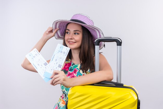 Mujer sonriente joven viajero con billetes de avión y maleta en pared blanca aislada