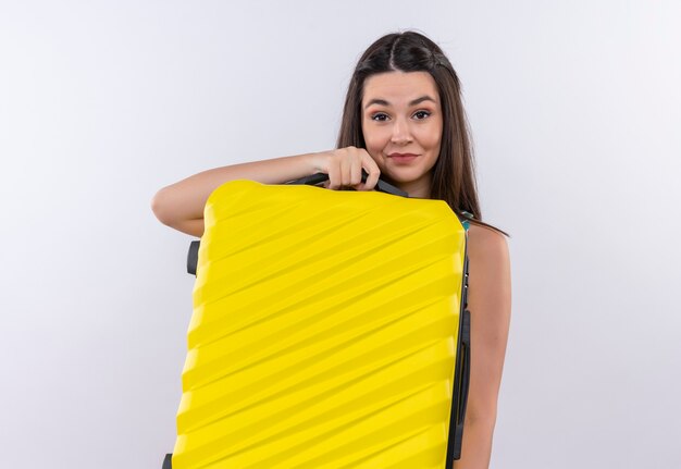 Mujer sonriente joven viajero con vestido multicolor sosteniendo una bolsa móvil en la pared blanca