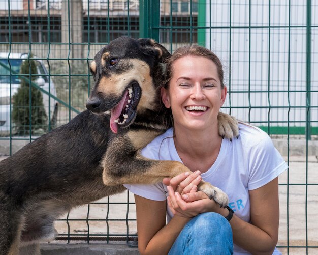 Mujer sonriente jugando en el refugio con perro esperando ser adoptado