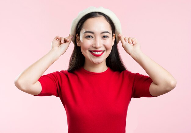 Mujer sonriente con labios rojos arreglando su sombrero