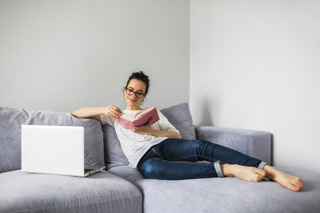 Mujer sonriente leyendo cerca de la computadora portátil