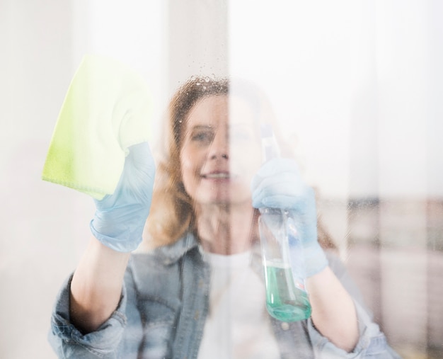 Mujer sonriente limpiando la ventana con un trapo