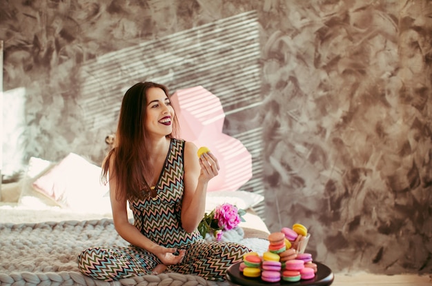 La mujer sonriente con los macarrones se sienta en cama