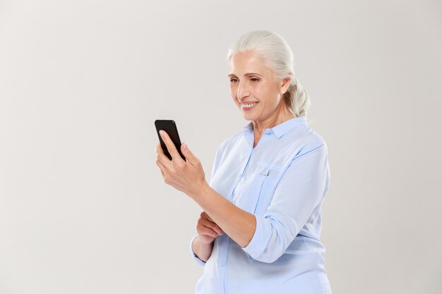 Mujer sonriente madura que usa el teléfono inteligente aislado