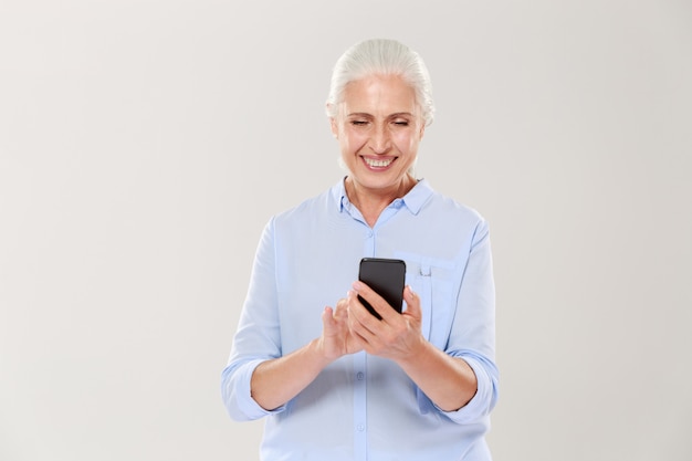 Mujer sonriente madura que usa el teléfono inteligente aislado