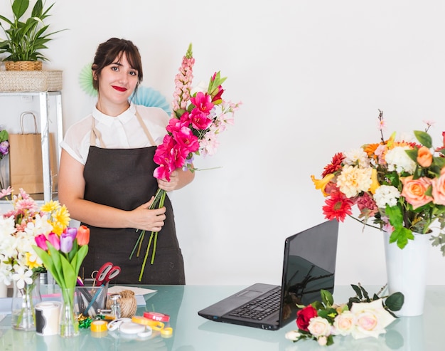Mujer sonriente con el manojo de flores que se colocan en tienda floral