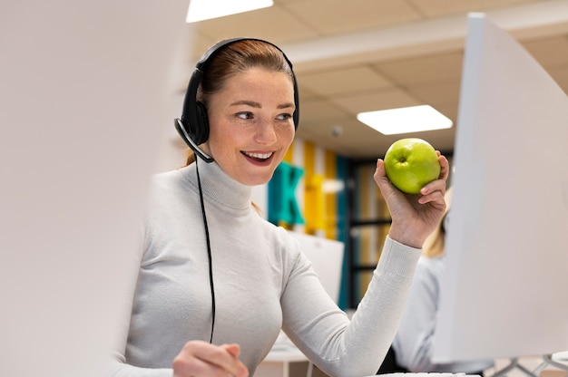Mujer sonriente con una manzana mientras trabaja en un centro de llamadas