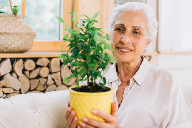 Una mujer sonriente mayor que sostiene la planta de tiesto