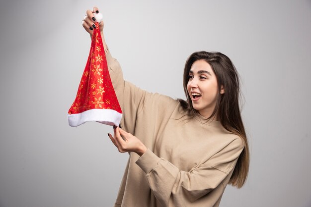 Mujer sonriente mirando el sombrero de Santa sobre un fondo gris.