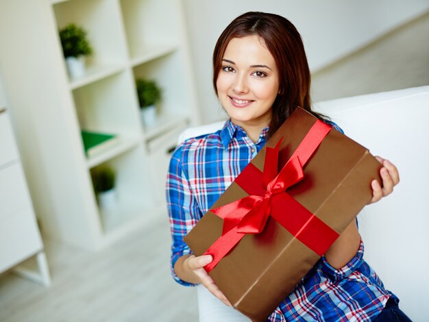 Mujer sonriente mostrando un regalo con un lazo rojo