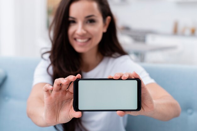 Mujer sonriente mostrando su teléfono con pantalla vacía