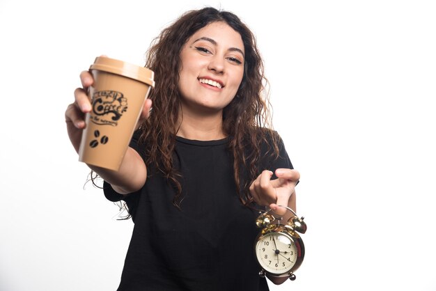 Mujer sonriente mostrando una taza de café con reloj sobre fondo blanco. Foto de alta calidad