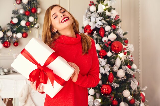 Mujer sonriente con muchas cajas de regalo posando cerca del árbol de Navidad decorado