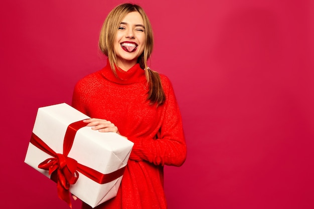 Mujer sonriente con muchas cajas de regalo posando en la pared roja