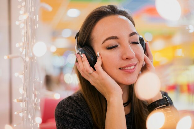 Mujer sonriente con los ojos cerrados con auriculares en la cabeza cerca de las luces de Navidad