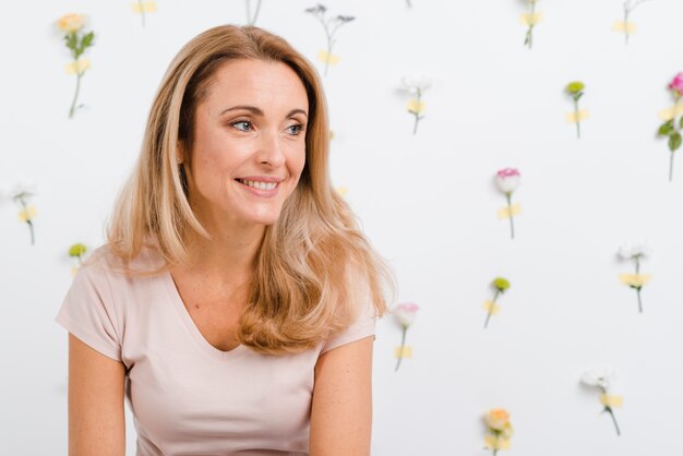 Mujer sonriente con pared de flores de primavera detrás