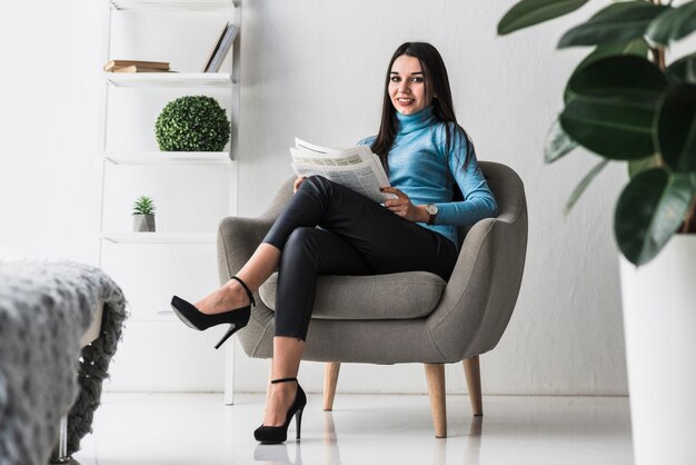 Mujer sonriente con periódico en sillón