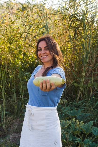 Mujer sonriente de pie en el campo mostrando calabaza cosechada