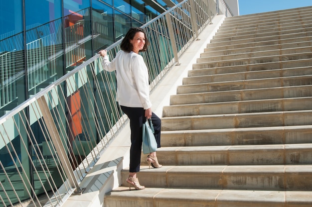 Mujer sonriente de pie en las escaleras, volviendo la cabeza hacia la cámara