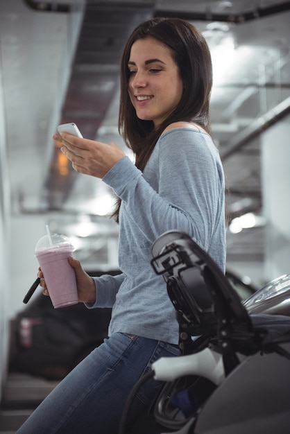 Mujer sonriente de pie junto a un coche y mediante teléfono móvil