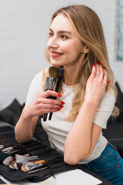 Mujer sonriente con pinceles de maquillaje en tocador