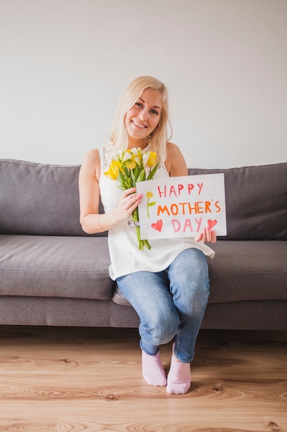 Mujer sonriente posando con un cartel y flores para el día de la madre