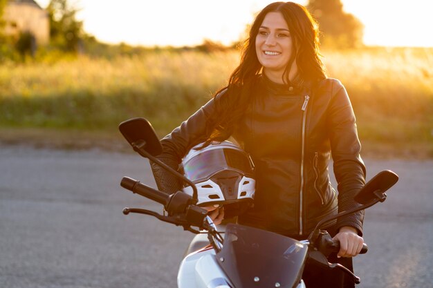Mujer sonriente posando con casco en su motocicleta