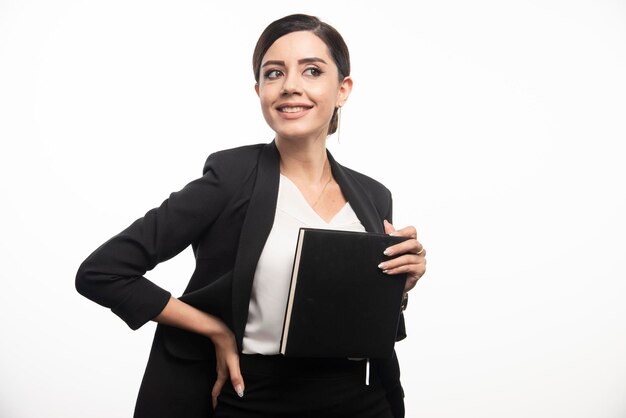 Mujer sonriente posando con cuaderno sobre fondo blanco. Foto de alta calidad