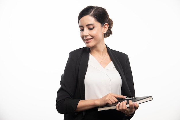 Mujer sonriente posando con cuaderno sobre fondo blanco. Foto de alta calidad