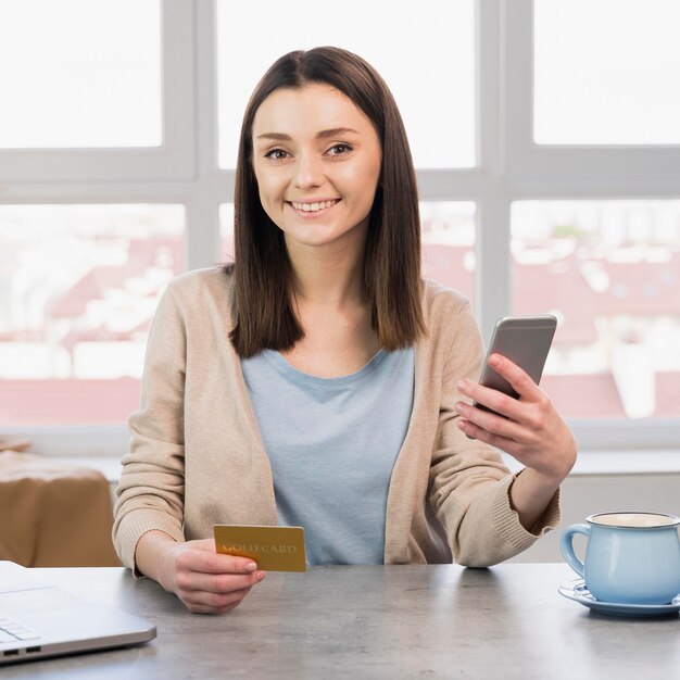 Mujer sonriente posando en el escritorio con teléfono inteligente