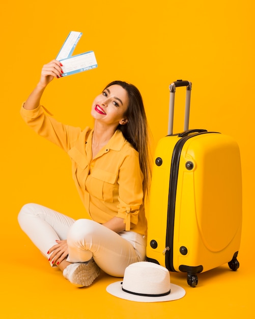 Mujer sonriente posando junto al equipaje mientras sostiene boletos de avión