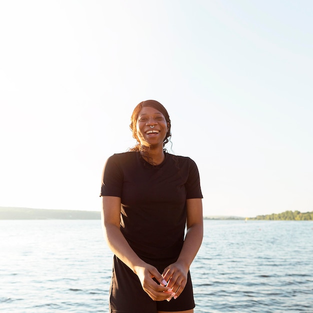 Mujer sonriente posando mientras hace ejercicio junto al lago